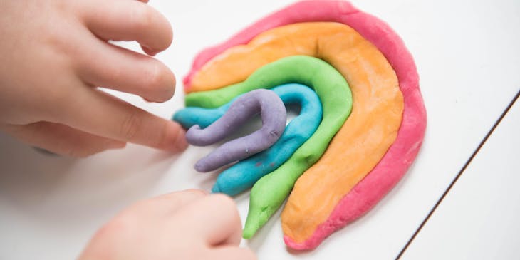 Las manos de un niño pequeño creando un arcoíris de plastilina.