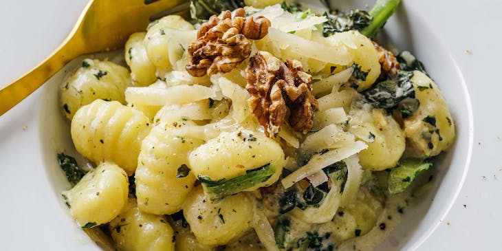 Un piatto di gnocchi con noci, formaggio e cime di rapa, sul tavolo di un ristorante italiano.