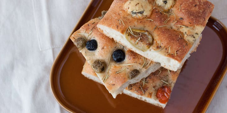 Tre fette di focaccia pugliese in un piatto marrone sopra un tavolo con una tovaglia bianca.