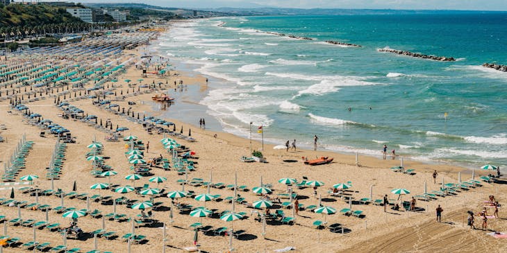 Uno stabilimento balneare con ombrelloni e sdraio blu e azzurre situato in un'ampia spiaggia con mare blu cristallino.