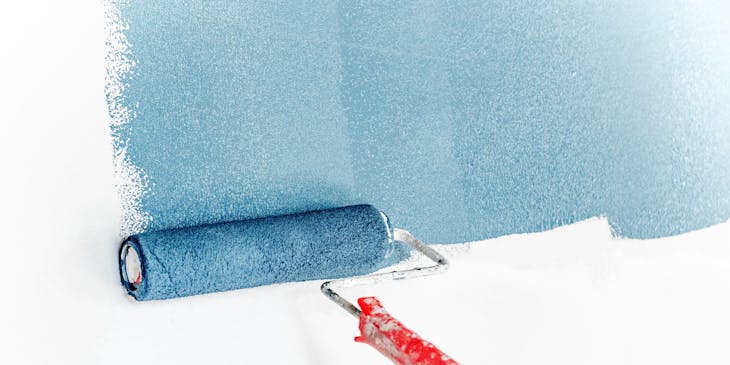 Capa de pintura azul que se aplica a una pared blanca con un rodillo en un negocio de pintura.