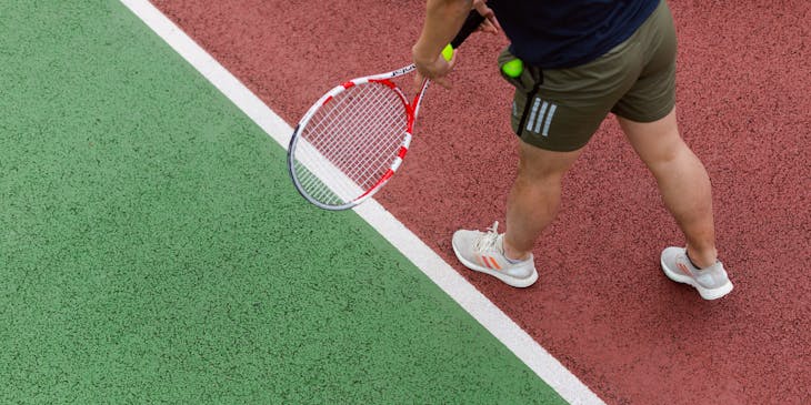 Entrenador de tenis con una raqueta de tenis y una pelota demostrando un servicio