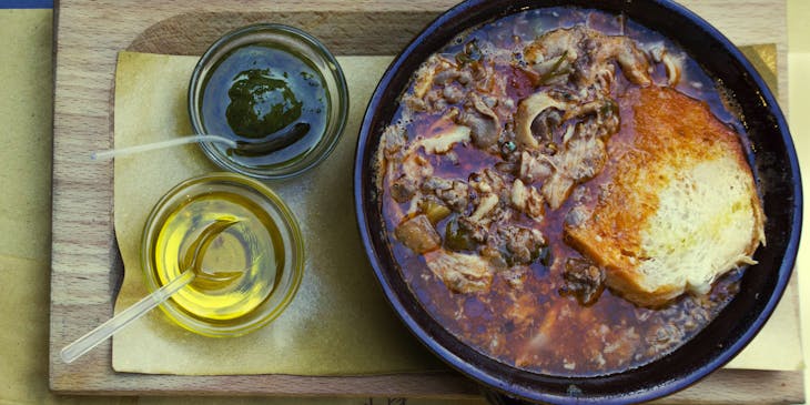 Un coccio di lampredotto e trippa al pomodoro con salsa verde e pane in una tripperia.