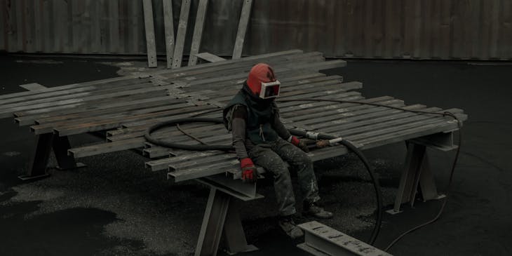 Un técnico sentado en barras de acero aplicando sandblasting en una empresa de sandblasting.