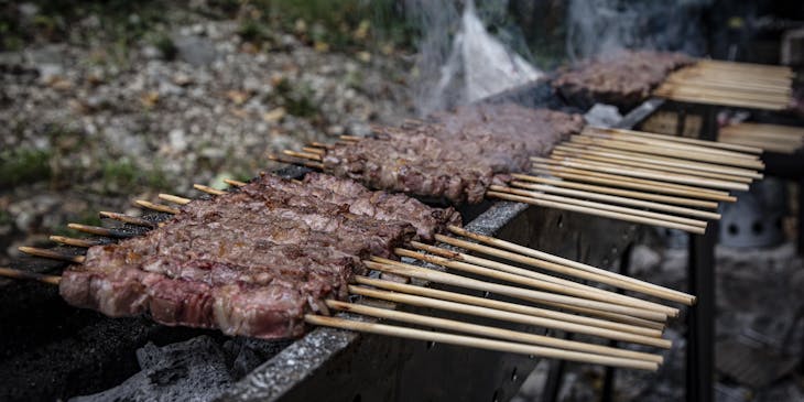 Una fila di arrosticini grigliati sopra una fornacella per arrosticini nel giardino di un ristorante di arrosticini.