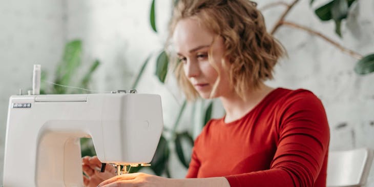 Una mujer trabajando en su máquina de coser ajustando el vestido de su cliente en una sastrería.