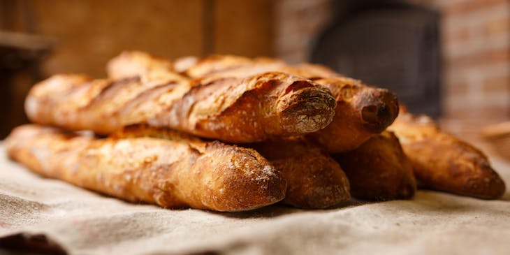 Panes franceses sobre un paño en una panadería con una estufa de leña al fondo.