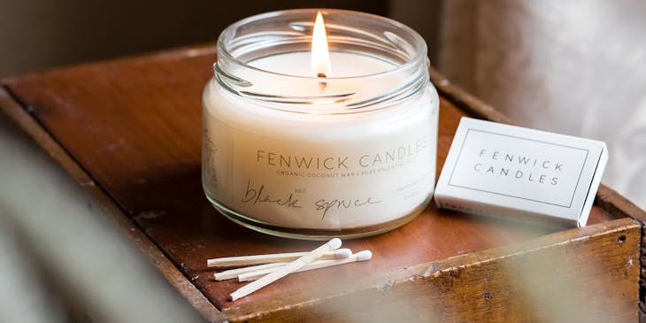 Burning white scented candle in a glass jar on a table.