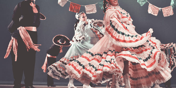 Hombres y mujeres vestidos con trajes típicos mexicanos bailando en una academia de danza folklórica.