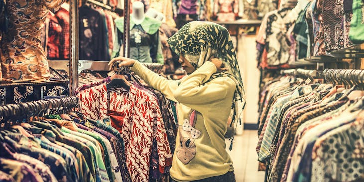 Mujer con mascada en la cabeza entre colgadores de ropa en un bazar de ropa usada.