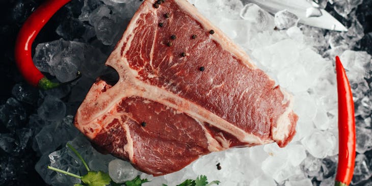 Un T-bone steak sobre una cama de hielo con dos chiles rojos, un manojo de cilantro y un cuchillo a su alrededor, en una boutique de carnes.