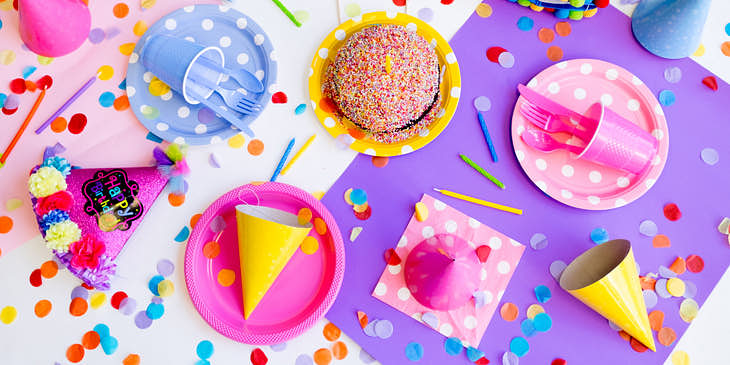 Gorros platos pastel velitas confeti cubiertos de plástico y un mantel en una casa de cumpleaños.