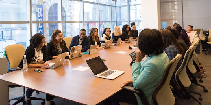 Sala de juntas de una consultora con personas reunidas y laptops sobre la mesa.