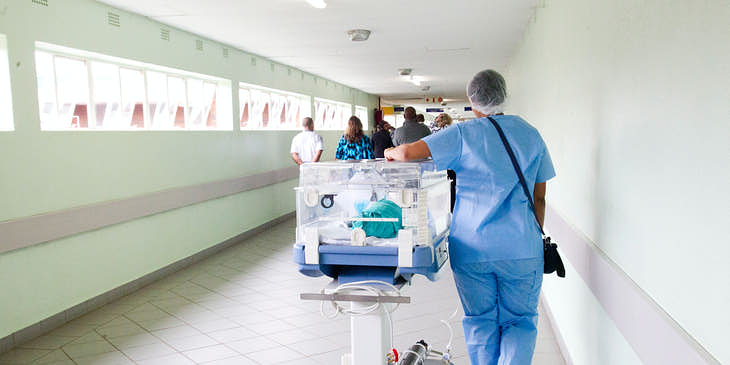 Una enfermera transportando a un bebé en una incubadora en un grupo de enfermería.