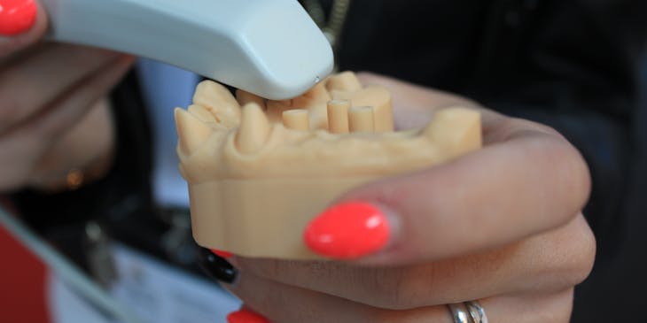 Empleada con las uñas pintadas de naranja sosteniendo una prótesis dental y un instrumento de laboratorio dental.