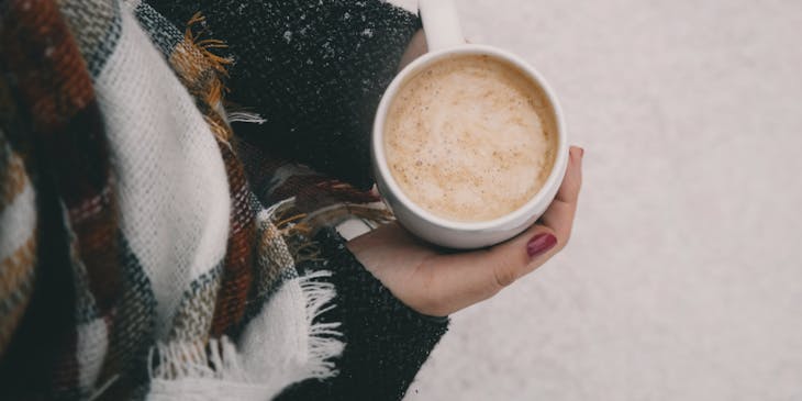 Una mujer sosteniendo una taza con atole con nieve de fondo en un negocio de atole.