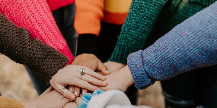 An agile team holding hands in an office huddle.