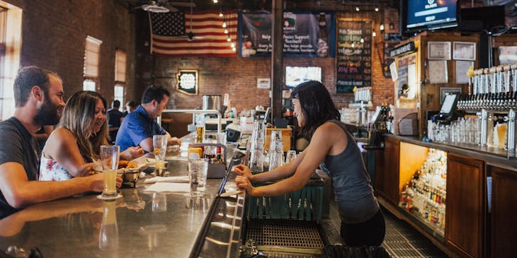 Woman taking drink orders from behind a bar counter in an American bar setting