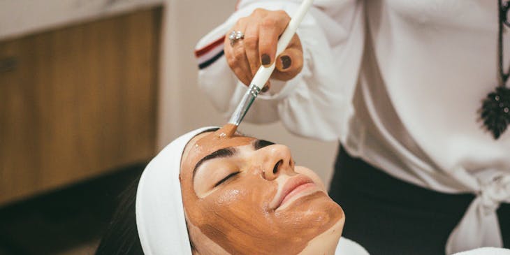 Una mujer recibiendo un facial de lodo en un centro de belleza.