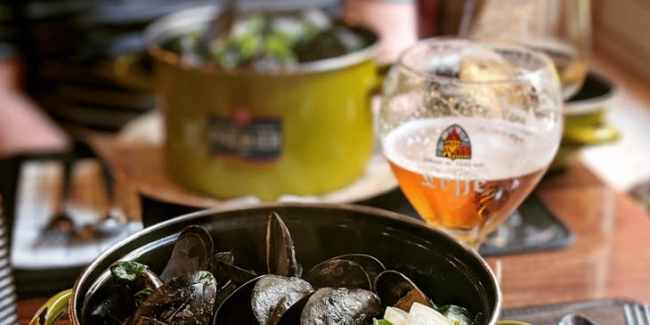 Un plat de moules belges dans une casserole à côté d'un verre de vin.