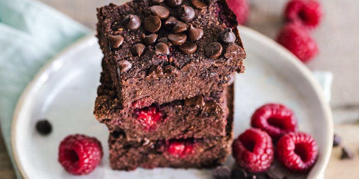 Tre brownies sopra un piatto guarniti con dei lamponi.