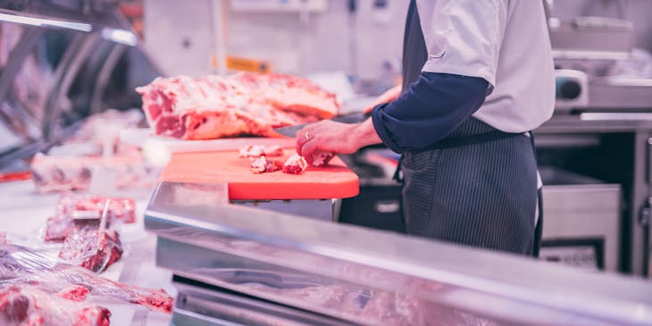 Açougueiro cortando carne crua em tamanhos pequenos em um açougue.