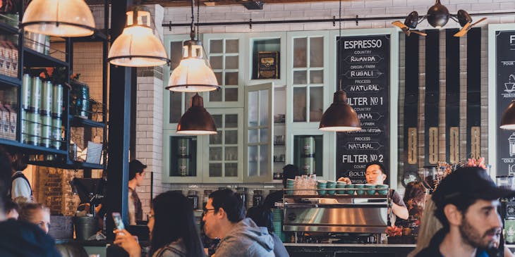 Un café con varias mesas llenas de personas disfrutando una bebida y una buena charla.