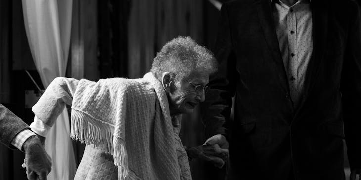 Dos personas de un negocio de cuidadores de adultos mayores que ayudan a caminar a una anciana.