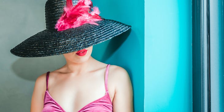 Una mujer en vestido rosa usando un sombrero negro con una flor rosa en una habitación de un negocio con clase.