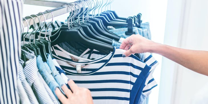 Mujer viendo camisetas colgadas en un colgador en un negocio de ropa.