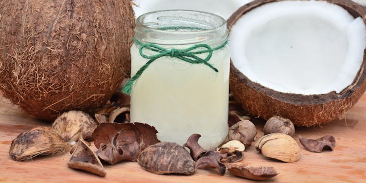 Un coco entero a un lado de un coco partido detrás de un frasco con aceite de coco sobre una mesa de madera en un negocio de coco.