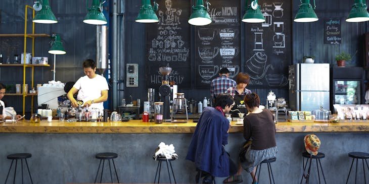 Clientes sentados en una barra con baristas sirviendo en una tienda de café.