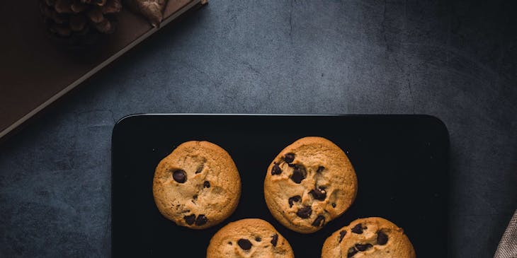 Four chocolate chip cookies in a black rectangular plate.