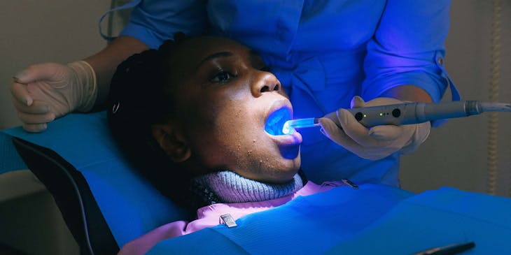 Dentista cosmético usando una lámpara de polimerización dental en un paciente en un negocio de dentistas cosméticos.