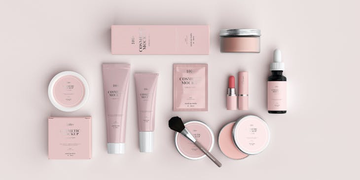 Insieme di cosmetici e accessori per il trucco, con packaging rosa sistemati con ordine su un piano bianco.