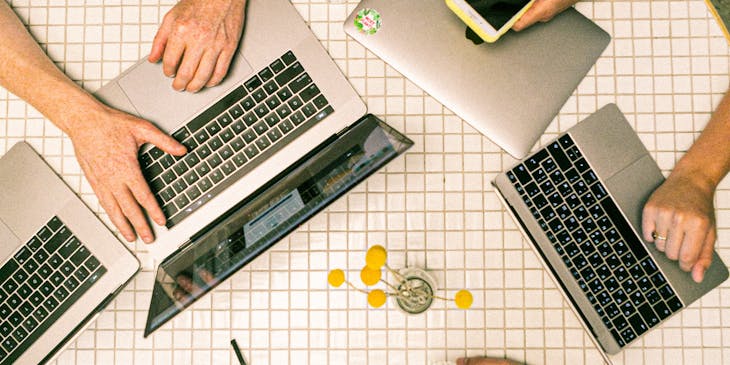 Desk full of laptops and working professionals in a coworking environment.