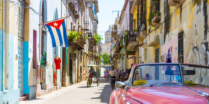 Uma típica rua de Cuba com um carro antigo rosa estacionado.