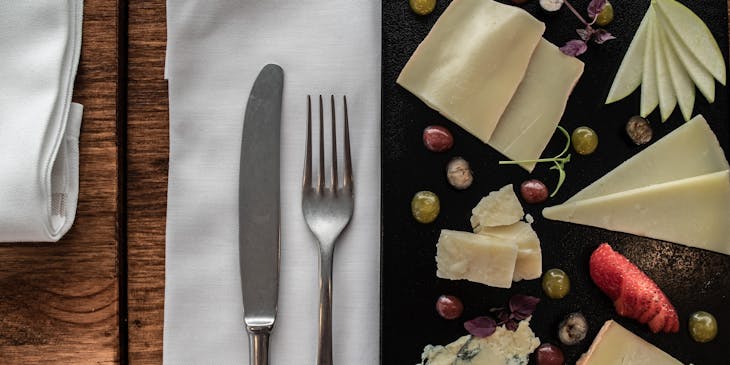 Couverts, y compris un couteau et une fourchette, placés sur une serviette en lin blanc sur une table entre une assiette avec un assortiment de fromages.