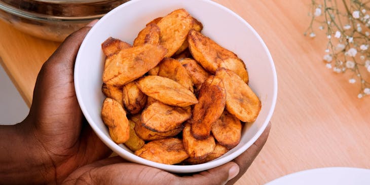 Las manos de una persona sosteniendo un bowl con plátanos fritos en un restaurante dominicano.