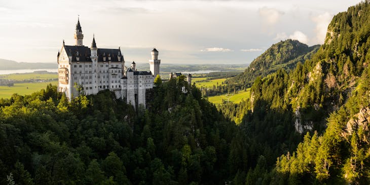 Un château blanc domine les arbres au sommet d'une montagne.