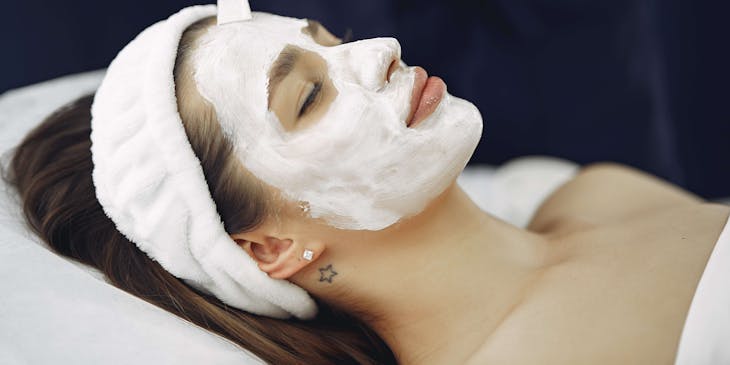 Esteticista colocando una mascarilla de arcilla blanca a una mujer.