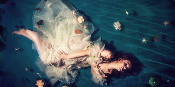 A woman wearing a white dress and posing against an ethereal background.