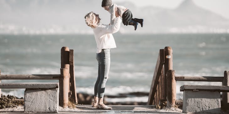 Una mamá cargando a su hijo en frente del mar en una playa durante una sesión de fotos de fotografía familiar