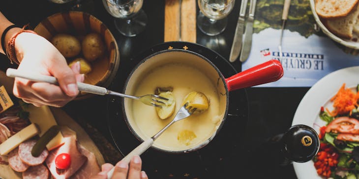 Dos personas sumergiendo pedazos de papa en una olla con queso fundido en un restaurante de fondue.