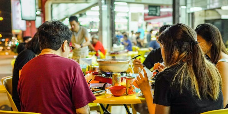 People sitting at a table in a food court eating food with their backs to the camera.