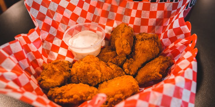 Basket of fried chicken on red and white napkin with a side of dressing.