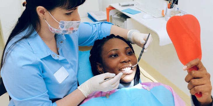 Paciente sendo atendida e sorrindo para um espelho em uma clínica odontológica.