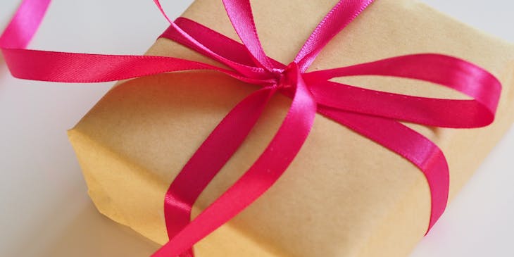 Una caja envuelta en papel marrón y decorada con una cinta rosa por un negocio de envolturas de regalos.