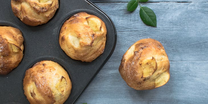 a freshly-baked apple muffin alongside a tray containing more muffins