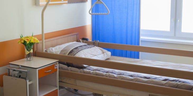 Un lit avec rembardes situé à côté d'un écran bleu dans un centre de soins palliatifs.